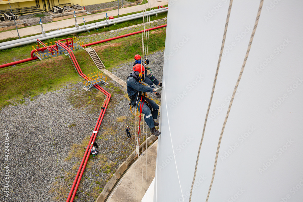 Male workers control swing rope down height white tank rope inspection of thickness tank.