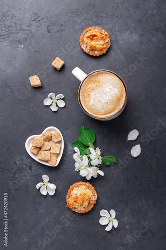Coffee, sweets and spring flowers on dark stone background. Top view