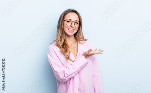 pretty caucasian woman smiling cheerfully, feeling happy and showing a concept in copy space with palm of hand