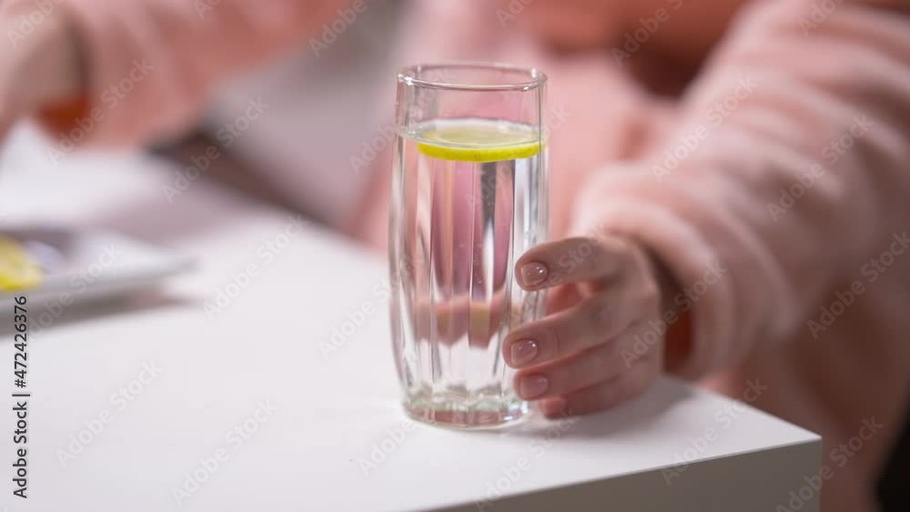 Close-up water with female hand putting lemon inside taking away glass in slow motion. Unrecognizable young Caucasian lady drinking detox cocktail at home in the morning Close-up water with female hand putting lemon inside taking away glass in slow motion. Unrecognizable young Caucasian lady drinking detox cocktail at home in the morning