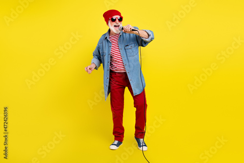 Full length body size view of attractive cheery funky grey-haired man singing hit rock isolated over bright yellow color background