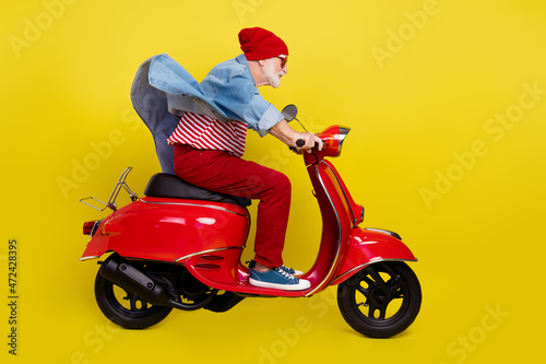 Profile side view portrait of elderly retired pensioner man riding moped having fun isolated over bright yellow color background © deagreez