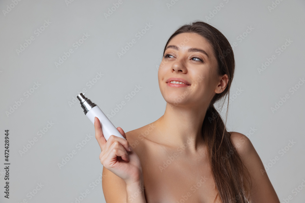 Young adorable happy girl in white towel using cosmetic oil, gel isolated over gray studio background. Natural beauty concept. Young adorable happy girl in white towel using cosmetic oil, gel isolated over gray studio background. Natural beauty concept.