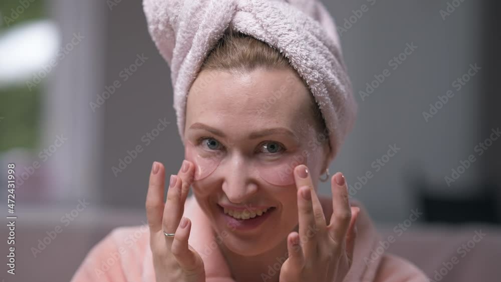 Front view laughing woman with eye patches looking at camera gesturing air kiss in slow motion. Portrait of carefree positive Caucasian lady in hair towel and bathrobe posing in the morning at home Front view laughing woman with eye patches looking at camera gesturing air kiss in slow motion. Portrait of carefree positive Caucasian lady in hair towel and bathrobe posing in the morning at home