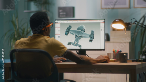 Black man using computer and creating 3D model of futuristic aircraft for videogame or movie while working from home photo