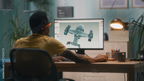 Black man using computer and creating 3D model of futuristic aircraft for videogame or movie while working from home