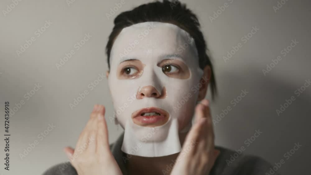 Multicultural brunette woman in bathrobe uses a cloth mask to moisturize her face. System of exercises improve skin yourself. Take care. Beauty procedures for yourself. Concept: personal grooming Multicultural brunette woman in bathrobe uses a cloth mask to moisturize her face. System of exercises improve skin yourself. Take care. Beauty procedures for yourself. Concept: personal grooming