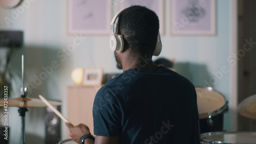 Billede på lærred Back view of African American musician in headphones playing drums during rehear