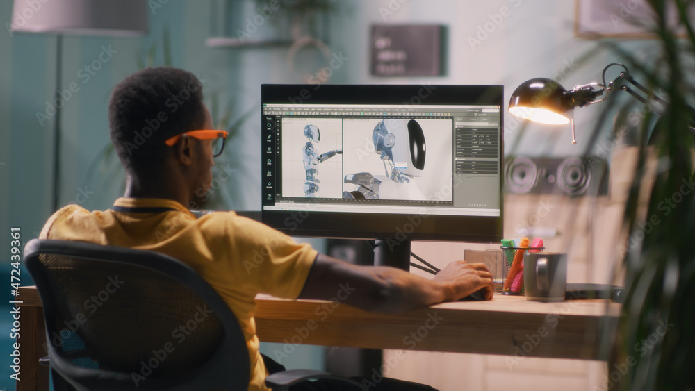 Black man in glasses and yellow t shirt sitting at table and using computer to create 3D model of futuristic robot for movie during work in home office - obrazy, fototapety, plakaty 