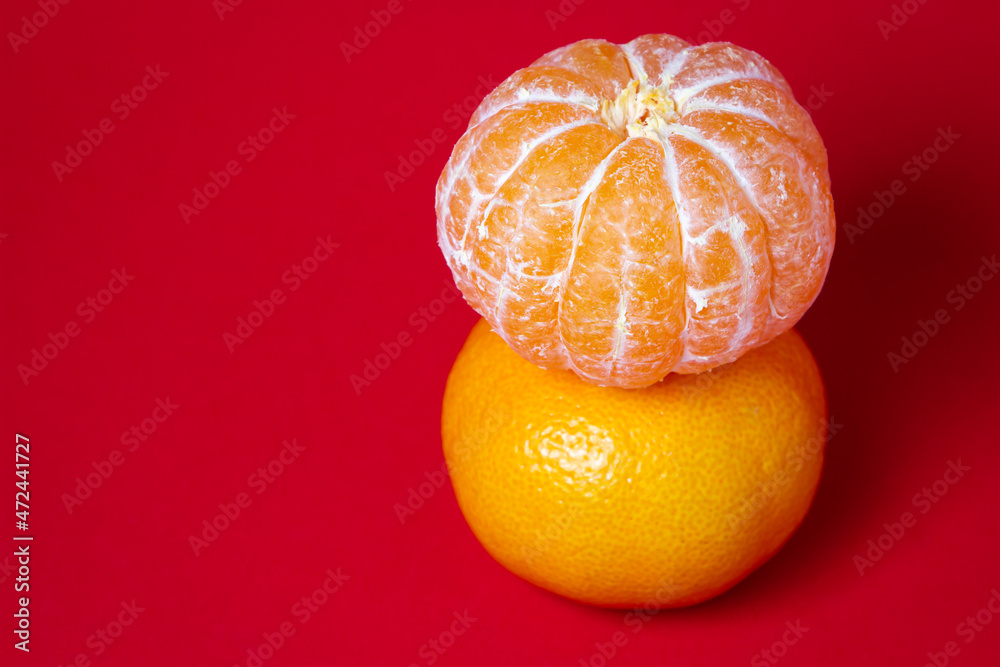 Peeled tangerine next to unpeeled tangerines on a red background. Citrus fruit on colored background Peeled tangerine next to unpeeled tangerines on a red background. Citrus fruit on colored background