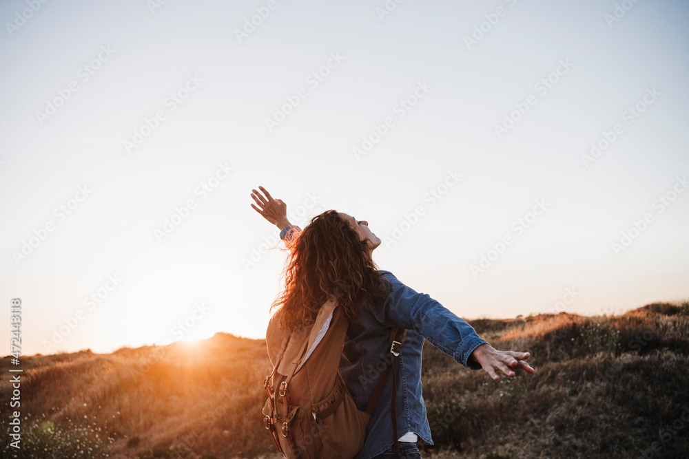 Carefree woman with backpack standing with arms outstretched in nature Carefree woman with backpack standing with arms outstretched in nature