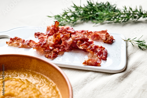 Roasted bacon for pumpkin cream soup with croutons in clay plate on the table with linen tablecloth. Autumn vegetable creamy soup puree. Healthy seasonal eating.