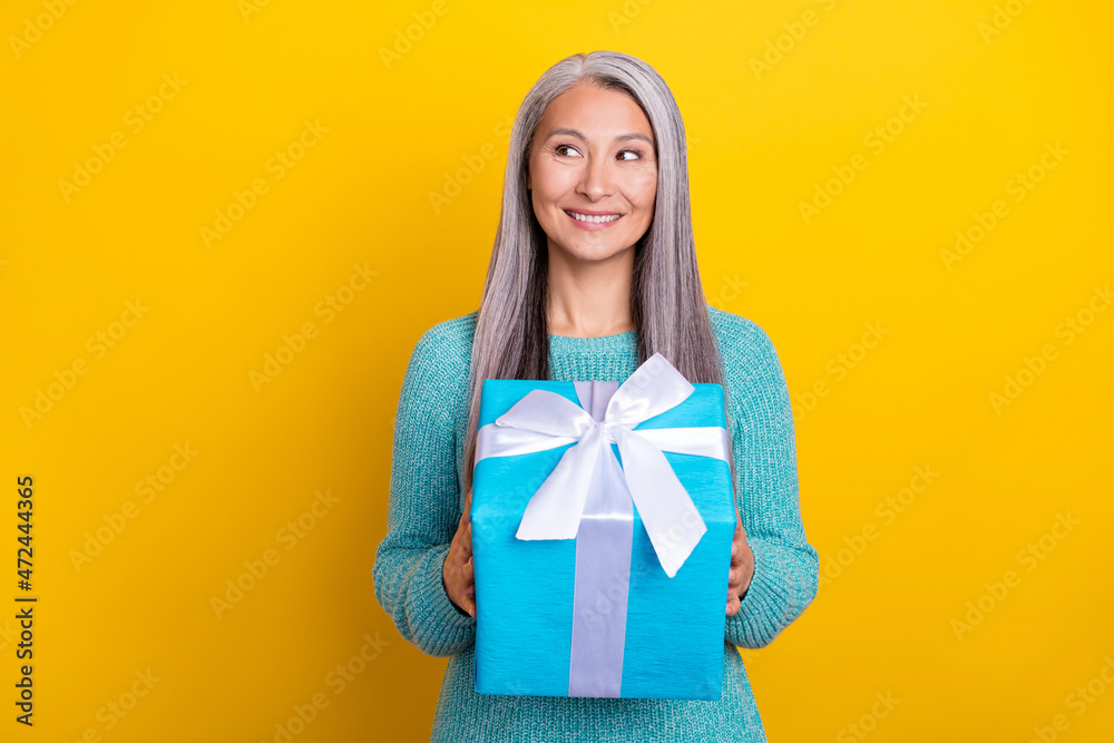 Photo of curious pretty mature woman look empty space dream gift box isolated over yellow color background Photo of curious pretty mature woman look empty space dream gift box isolated over yellow color background