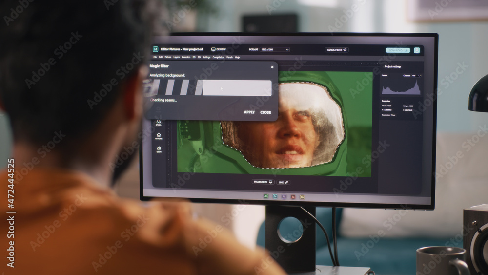 Back view of unrecognizable male retouching astronaut photo on computer while sitting at table and working in workplace at home Back view of unrecognizable male retouching astronaut photo on computer while sitting at table and working in workplace at home