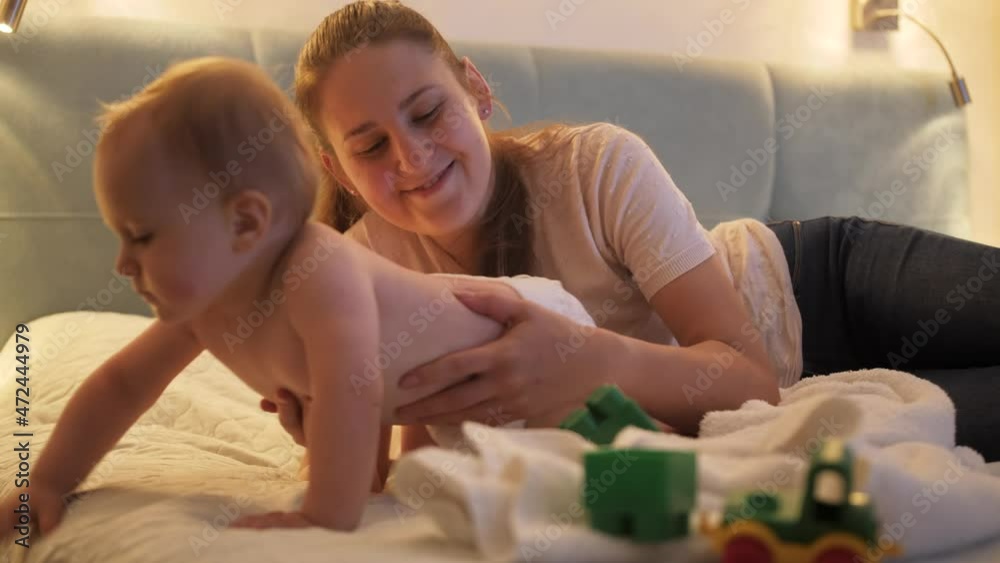 Cute baby boy crawling away from mother on bed at night. Concept of parenting, child development and family having time together. Cute baby boy crawling away from mother on bed at night. Concept of parenting, child development and family having time together.