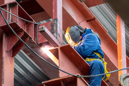 A welder with a protective mask for welding metal and sparks performs welding work on a construction site.