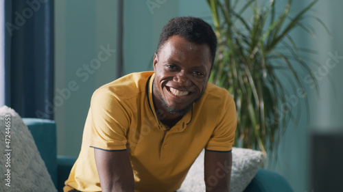 Happy African American man looking at camera with smile and clenching fists while sitting on sofa and celebrating victory at home