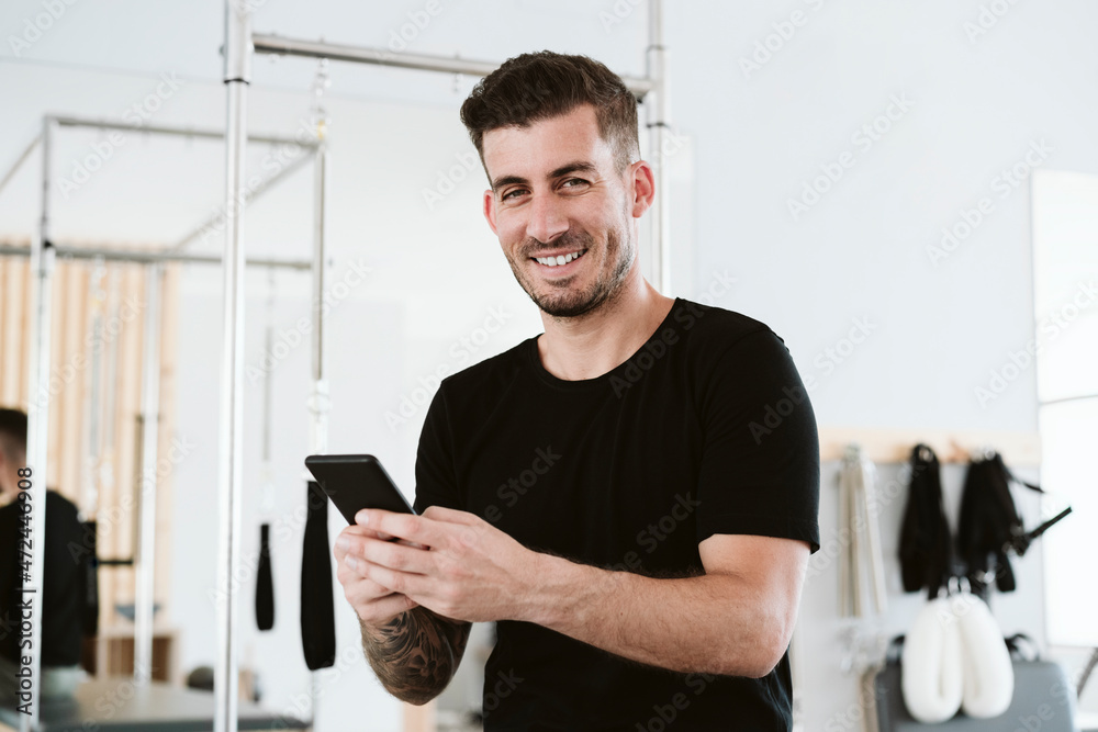 Smiling male owner holding smart phone in pilates studio Smiling male owner holding smart phone in pilates studio