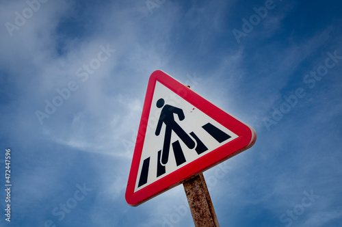 Pedestrian crossing sign against a blue sky, red triangle.