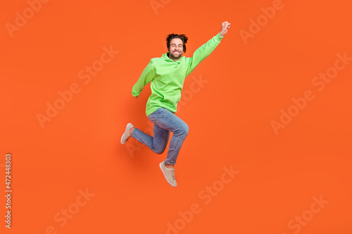 Full size photo of brunet young guy jump save world wear sweater jeans sneakers isolated on orange background