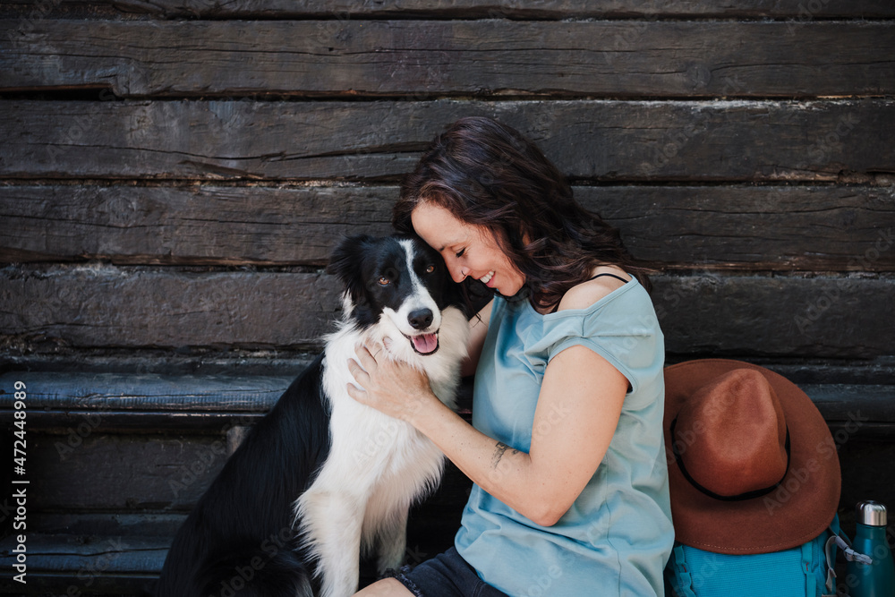 Smiling woman with eyes closed embracing dog while sitting in front of cottage Smiling woman with eyes closed embracing dog while sitting in front of cottage