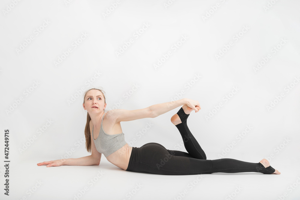 Young slender woman does yoga or gymnastics. Girl does an exercise to improve flexibility on white background.