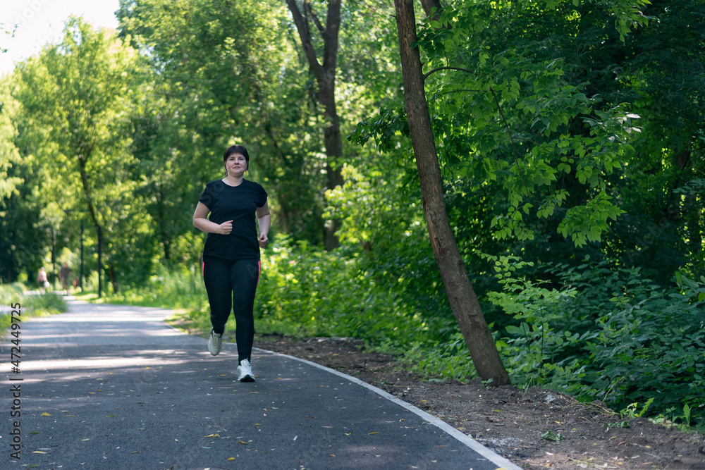 Young woman with weight excess runs in the park. Girl with curvy figure goes in for sports to lose extra pounds. Young woman with weight excess runs in the park. Girl with curvy figure goes in for sports to lose extra pounds.