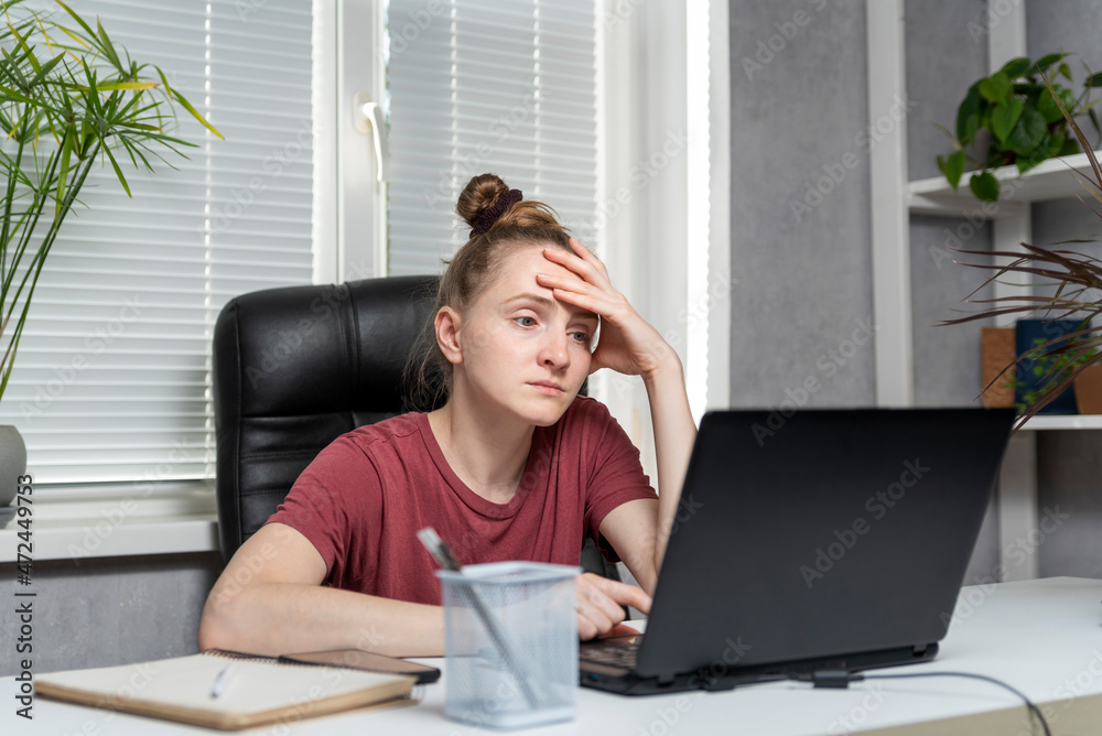Young woman freelancer works from home. Girl sits at the workplace, works at laptop, tired of taking up her head. Young woman freelancer works from home. Girl sits at the workplace, works at laptop, tired of taking up her head.