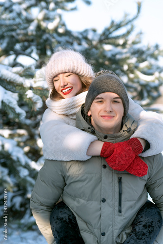 Laughing girl riding on the back of a guy. Lovers have fun in the winter forest