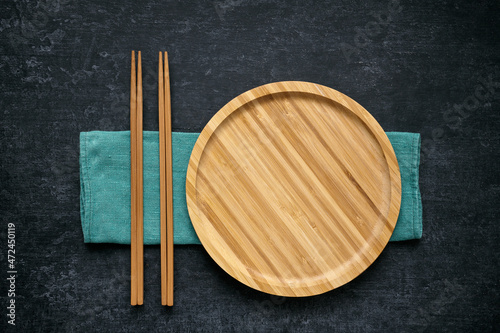 Large flat empty bamboo plate and chopsticks lie on green linen napkin