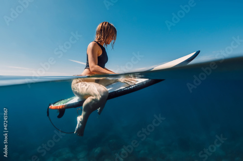 Sunny day with attractive surf girl waiting waves on surfboard in sea.