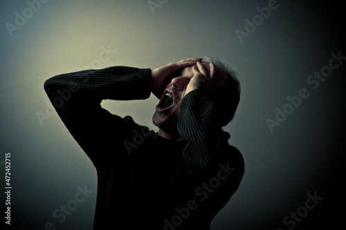 man with hands on his head screaming, concept for madness and insanity