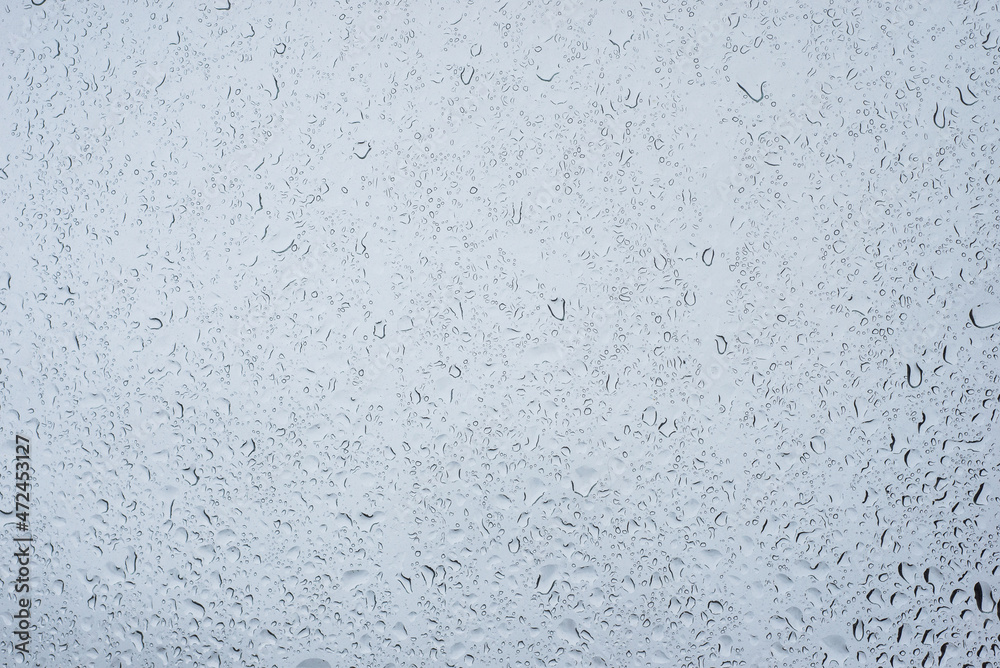 Closeup of rain drops on window on grey sky background