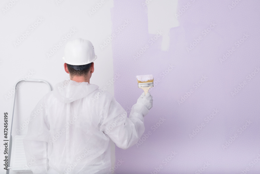 man in protective clothing and hard hat paints a white wall man in protective clothing and hard hat paints a white wall