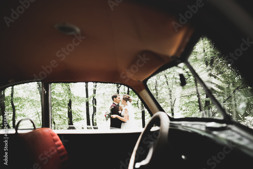 Beautiful newlywed couple posing near retro black car