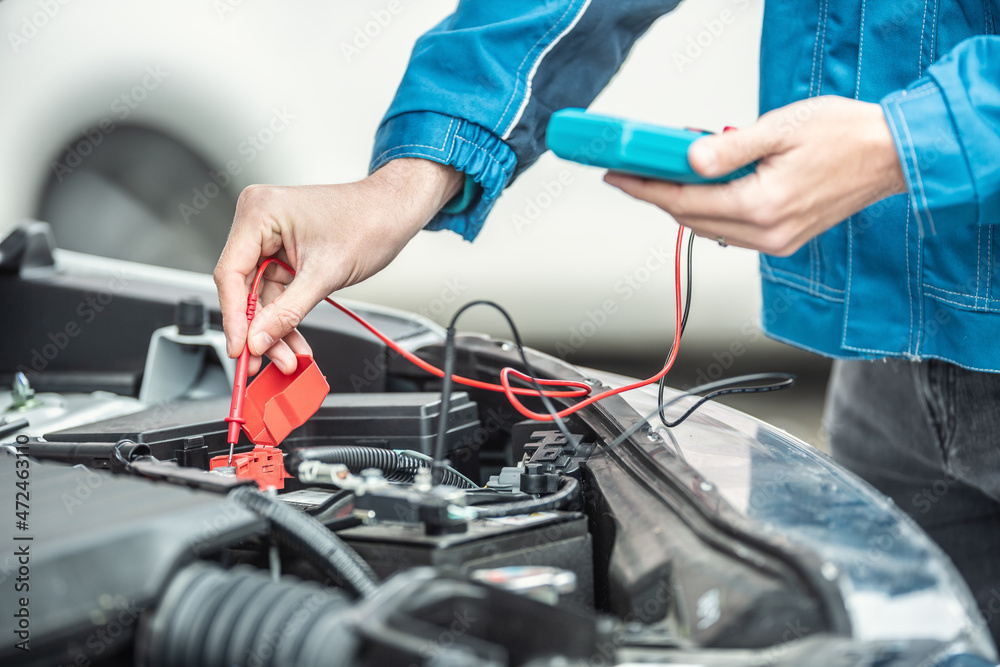 Car electrician or mechanic checks voltage in car battery inside the