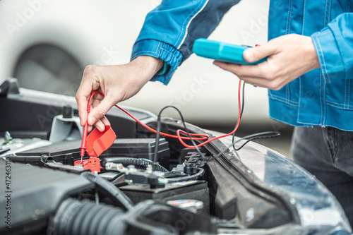 Car electrician or mechanic checks voltage in car battery inside the car engine with open hood