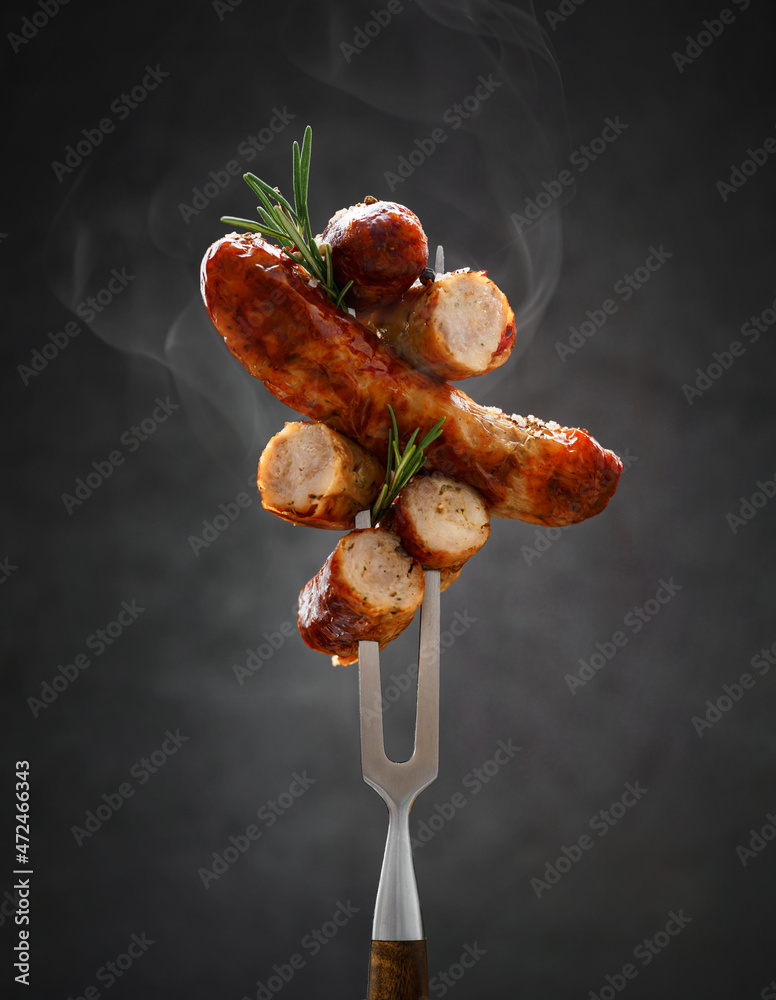 a whole and sliced grilled hot fried sausage is strung on a meat fork