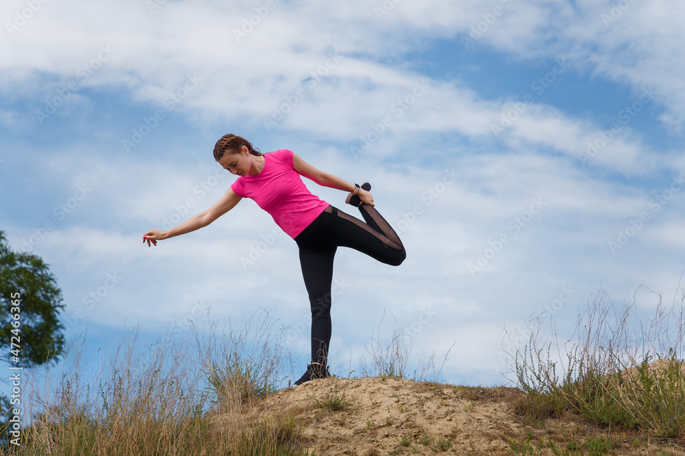 Young sporty woman in sportswear on hill top stretching, warming up or doing yoga on cloudy sky background. Fitness, healthy way of life, wellbeing, freedom, loosing weight concept. Young sporty woman in sportswear on hill top stretching, warming up or doing yoga on cloudy sky background. Fitness, healthy way of life, wellbeing, freedom, loosing weight concept.