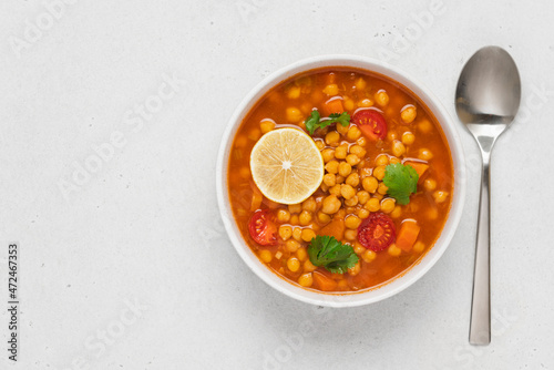 Chickpea lentil soup with vegetables, cilantro and lemon in light bowl on white table. Vegetarian soup top view