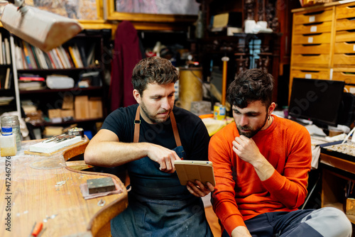 Two brothers looking at ideas and references on a digital tablet to work together in their craft workshop.