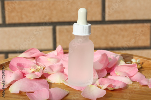 Clear bottle with white dropper for mock up. A beauty product bottle standing on a rose petals. Idea for rose natural cosmetics