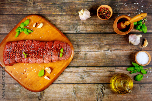 Uncooked beef fillet with herbs and spices on wooden table.