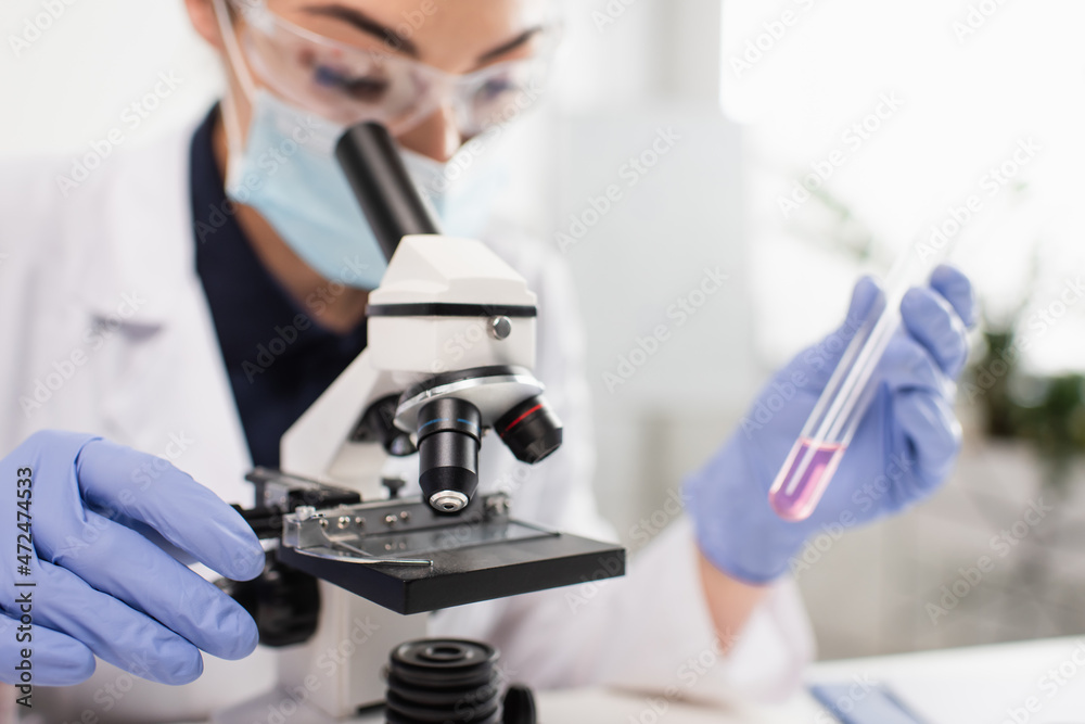 Microscope near scientist in latex gloves holding test tube in lab. Microscope near scientist in latex gloves holding test tube in lab.