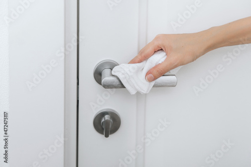 Cleaning black door handles with an antiseptic wet wipe. Sanitize surfaces prevention in hospital and public spaces against corona virus. Woman hand using towel for cleaning.