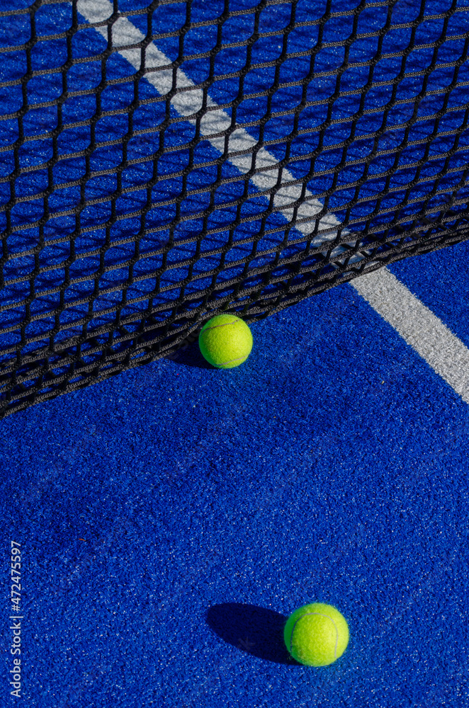 Two balls by the net of a paddle tennis court