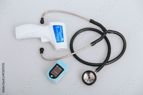 Stethoscope, pulse oximeter and thermometer gun on white background. Phonendoscope. Infrared isometric thermometer gun to check body temperature for virus symptoms. Treatment of cold or flu.