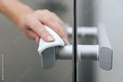 Cleaning glass door handles with an antiseptic wet wipe. Sanitize surfaces prevention in hospital and public spaces against corona virus. Woman hand using towel for cleaning home room door link.