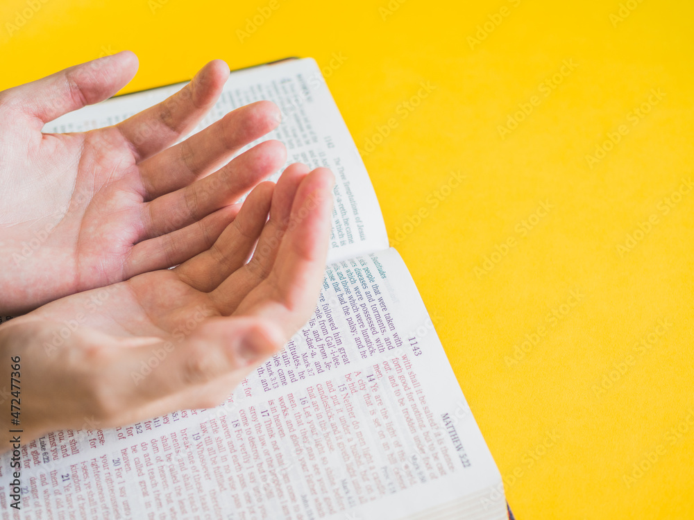 Obraz premium Hands on holy bible with copy space on yellow background.