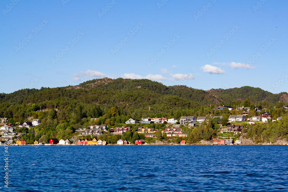Colorful traditional Norwegian houses near the sea with green forest on mountains and blue sky